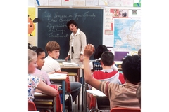 A child raises his hand while sitting in the back of the classroom.